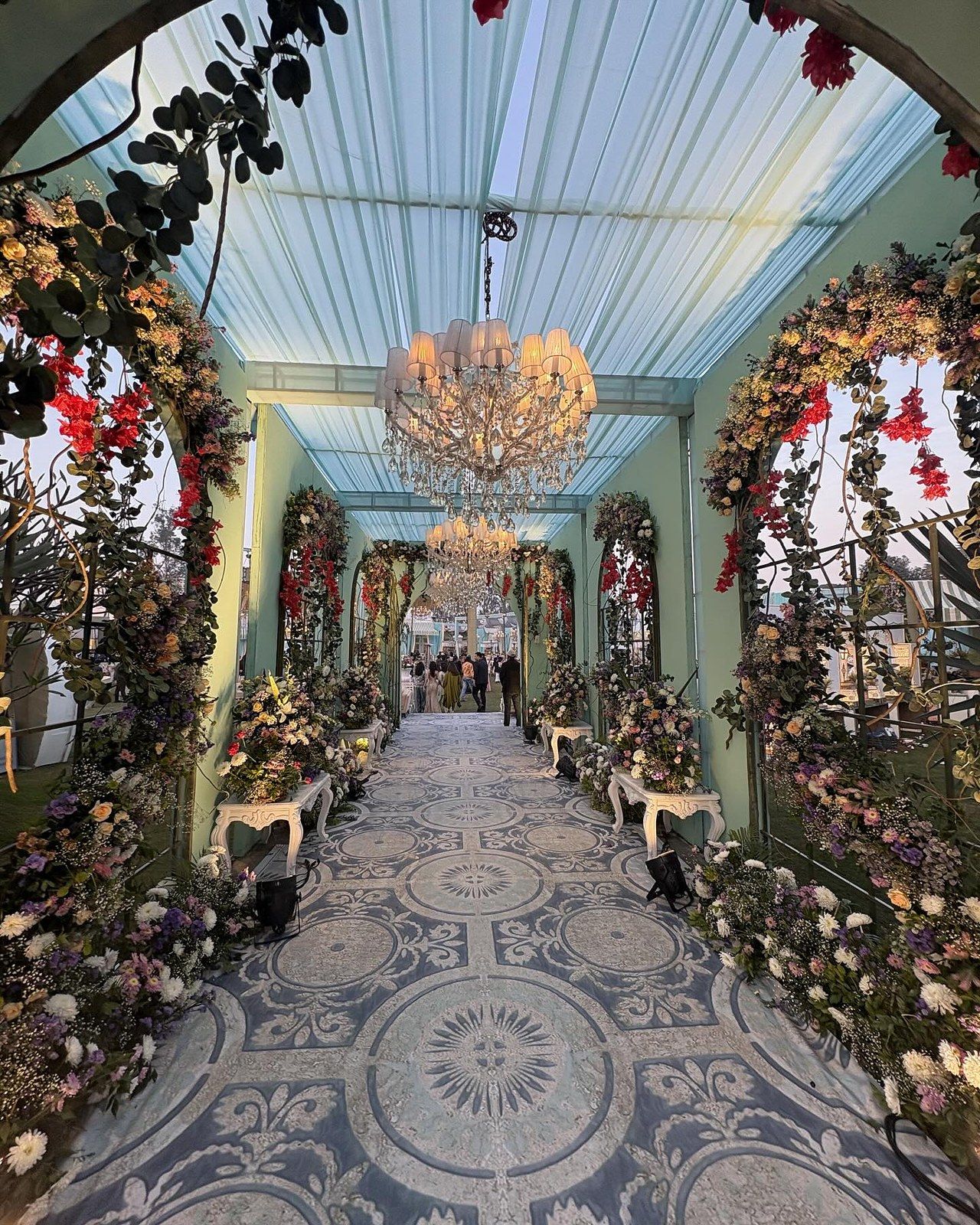 A long floral tunnel with chandeliers and a patterned floor, seen end to end