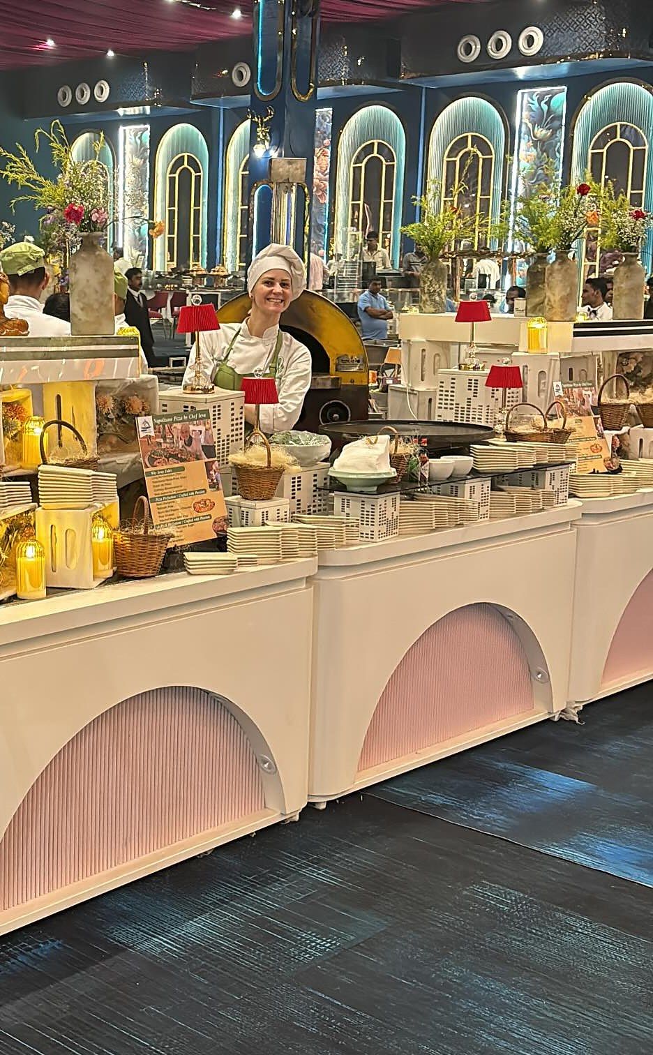 A pink counter with arched fronts, lamps and florals, and a chef behind it