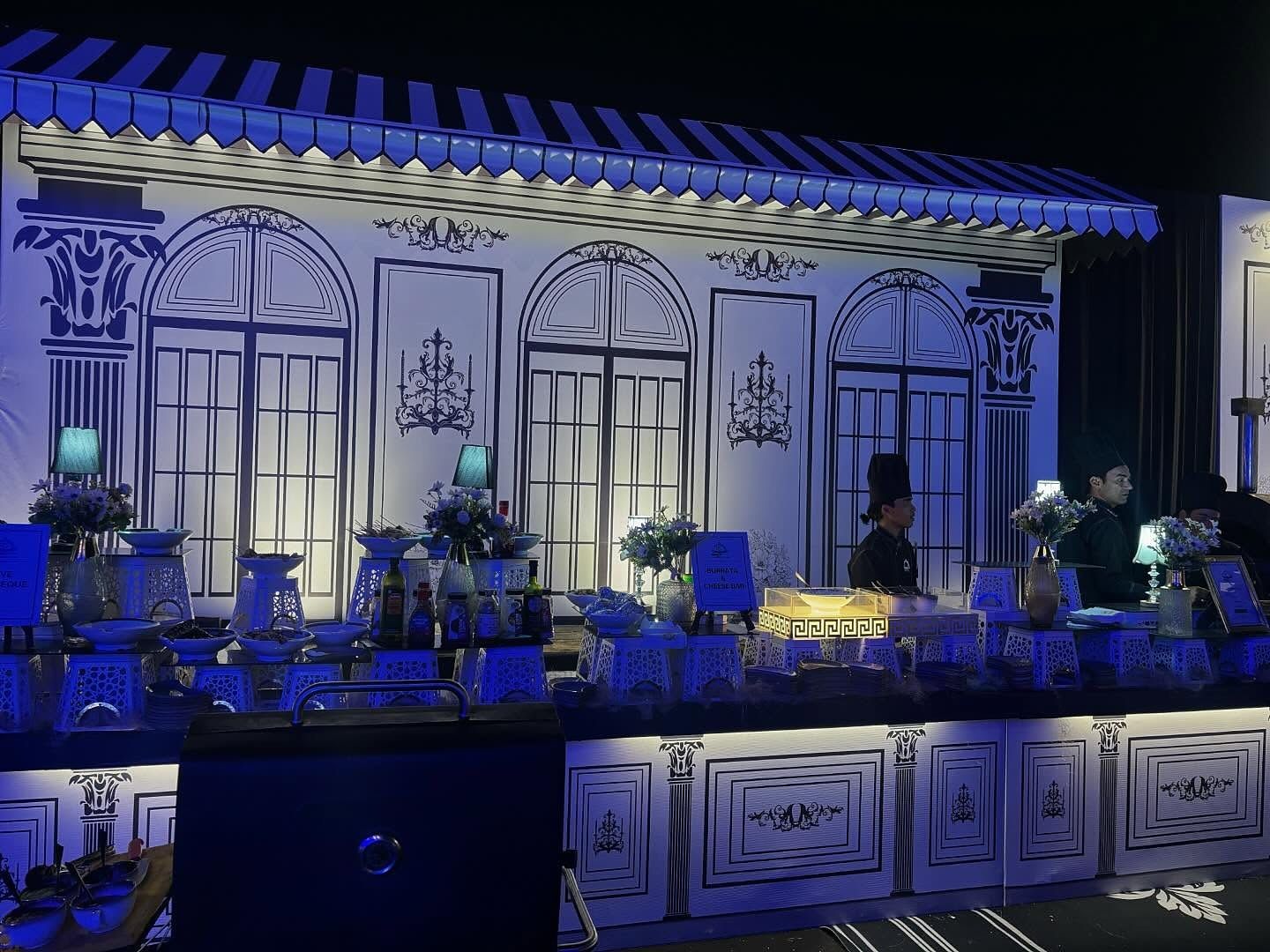A counter built as a striped-awning facade, lit blue at night, with two chefs