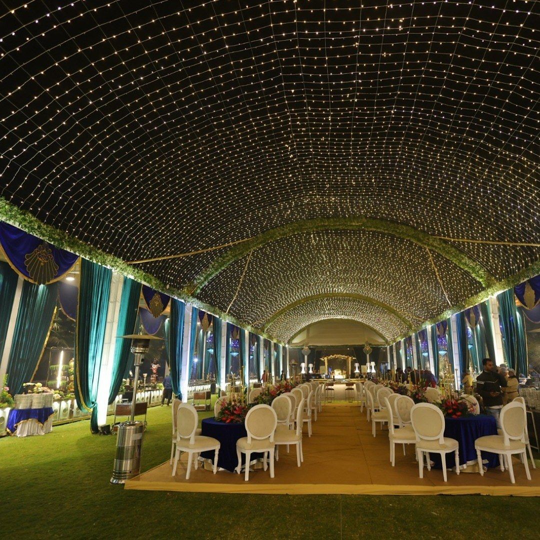 A tunnel of fairy lights over a lawn set with round tables and white chairs