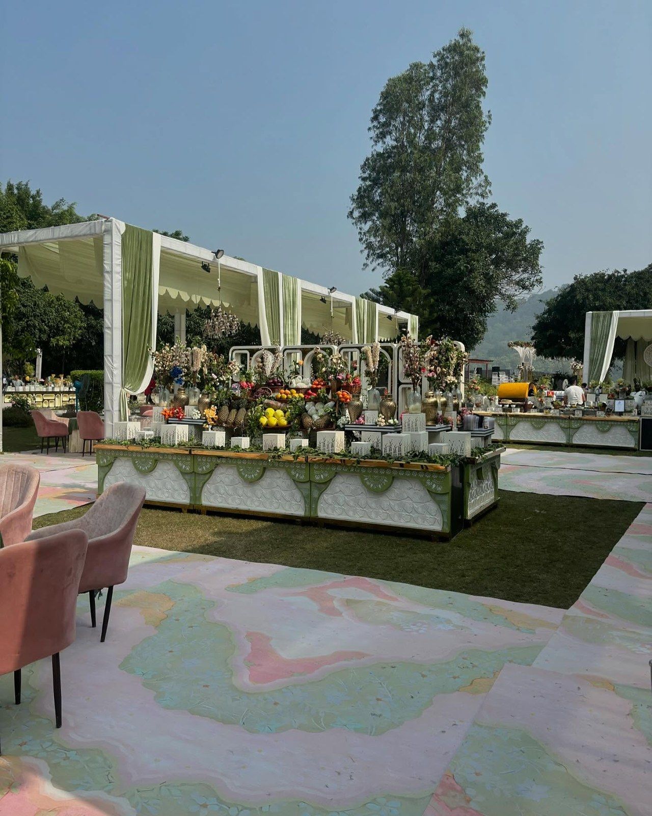A lawn event set on a pastel painted floor with a green-draped counter and trees behind