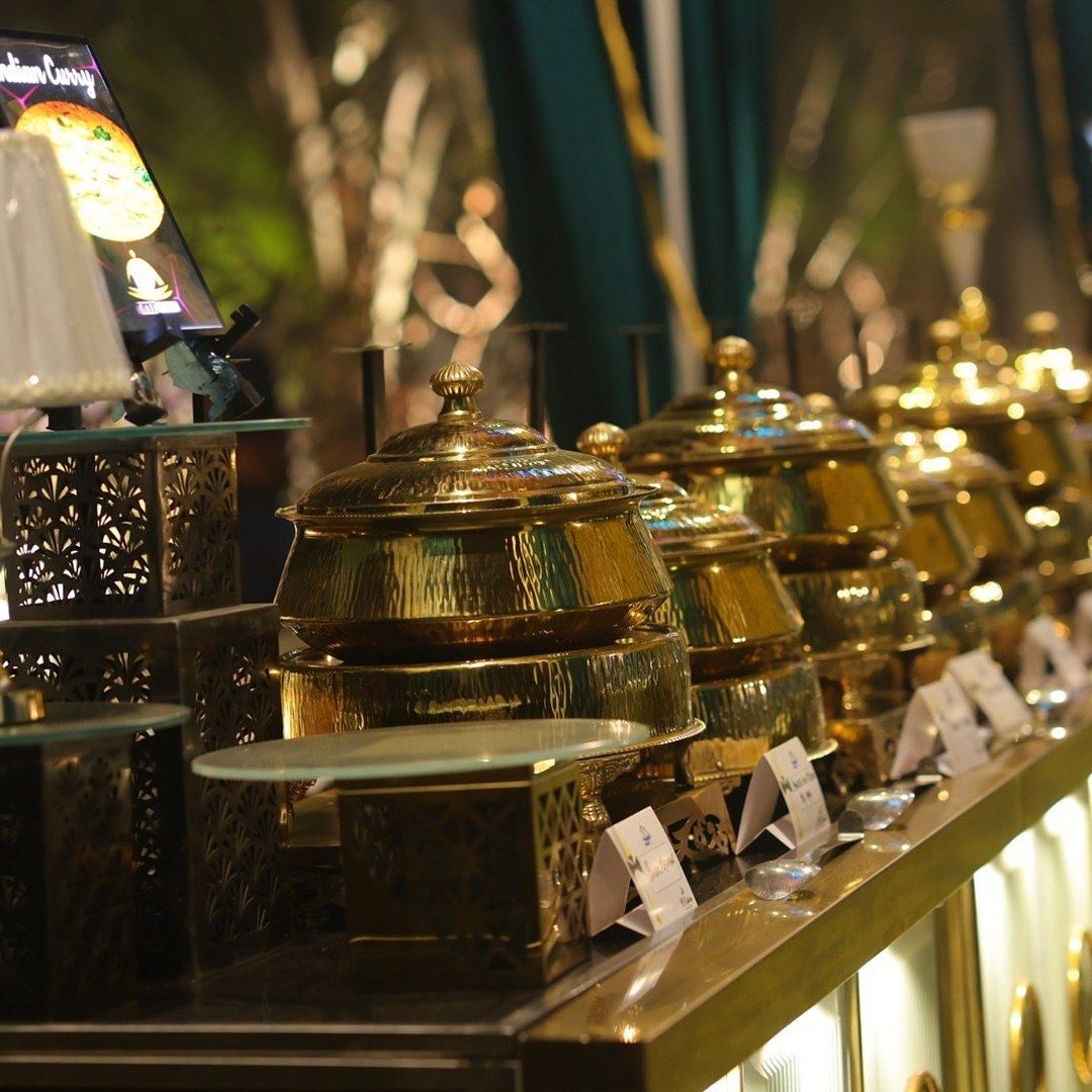 A row of brass handis with lids on a lit counter, menu cards in front