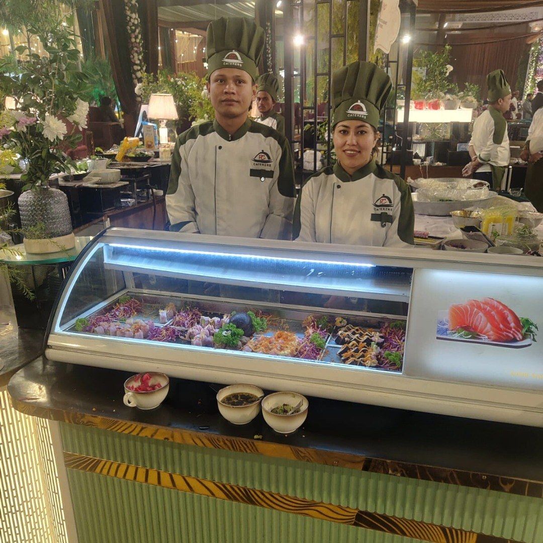 Two chefs in green toques behind a chilled sushi display