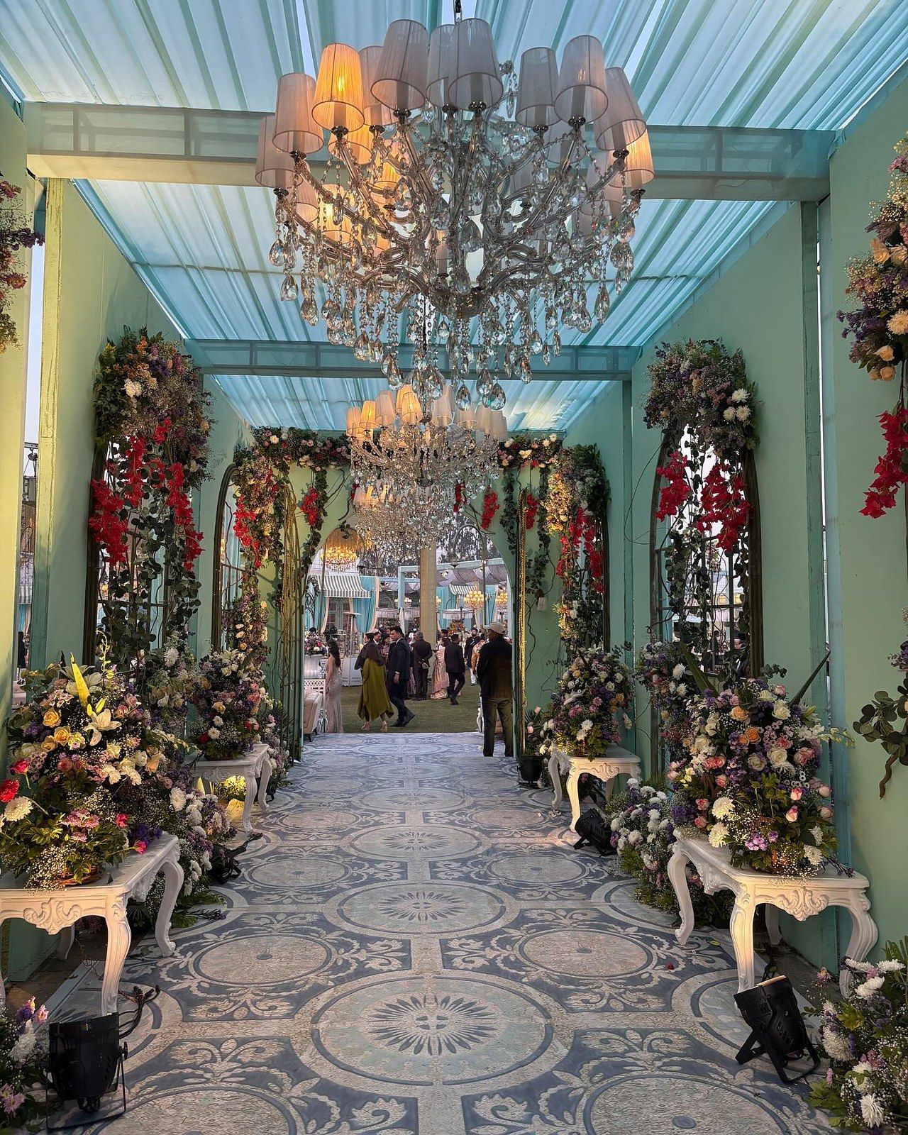 Looking up at a chandelier in a floral tunnel, with guests at the far end