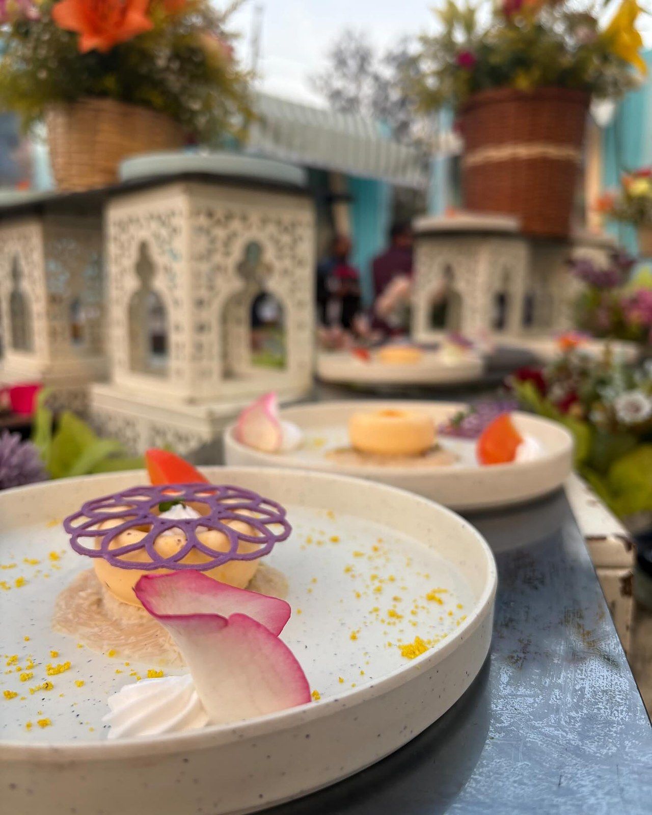 A plated dessert with a purple lattice, a rose petal and gold crumb on a white plate