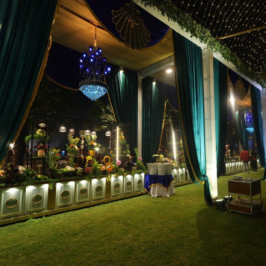 A green-draped tent with a blue chandelier and lit counters along the lawn