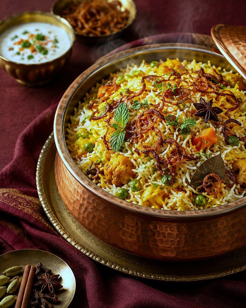 Illustration of vegetable dum biryani in a copper handi, with raita on the side